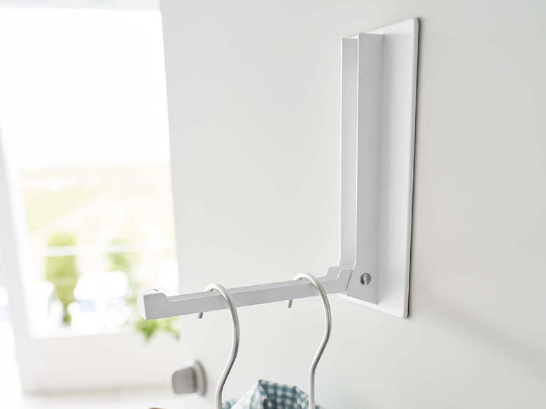 ホワイトのマグネット折り畳みハンガーが壁に設置され、衣類や電気ケーブルが掛けられている様子