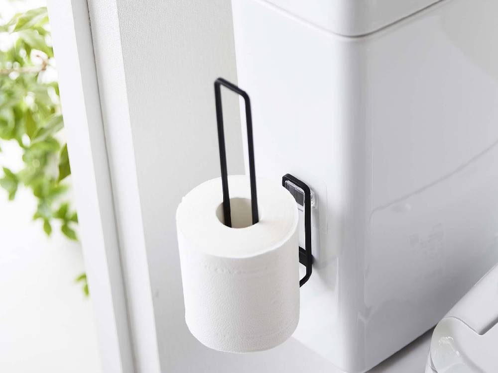 白色のスチール製トイレットペーパーホルダーが浴室のタイル壁に取り付けられており、ペーパータオルホルダーと石鹸ディスペンサーも見えます。