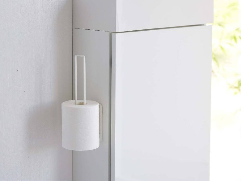 スチール製タワーデザインのフィルムフックトイレットペーパーホルダーがバスルームのタイル壁に取り付けられており、トイレットロール2本がセットされている様子。周囲には紙タオルホルダーや石鹸ディスペンサーも配置されている