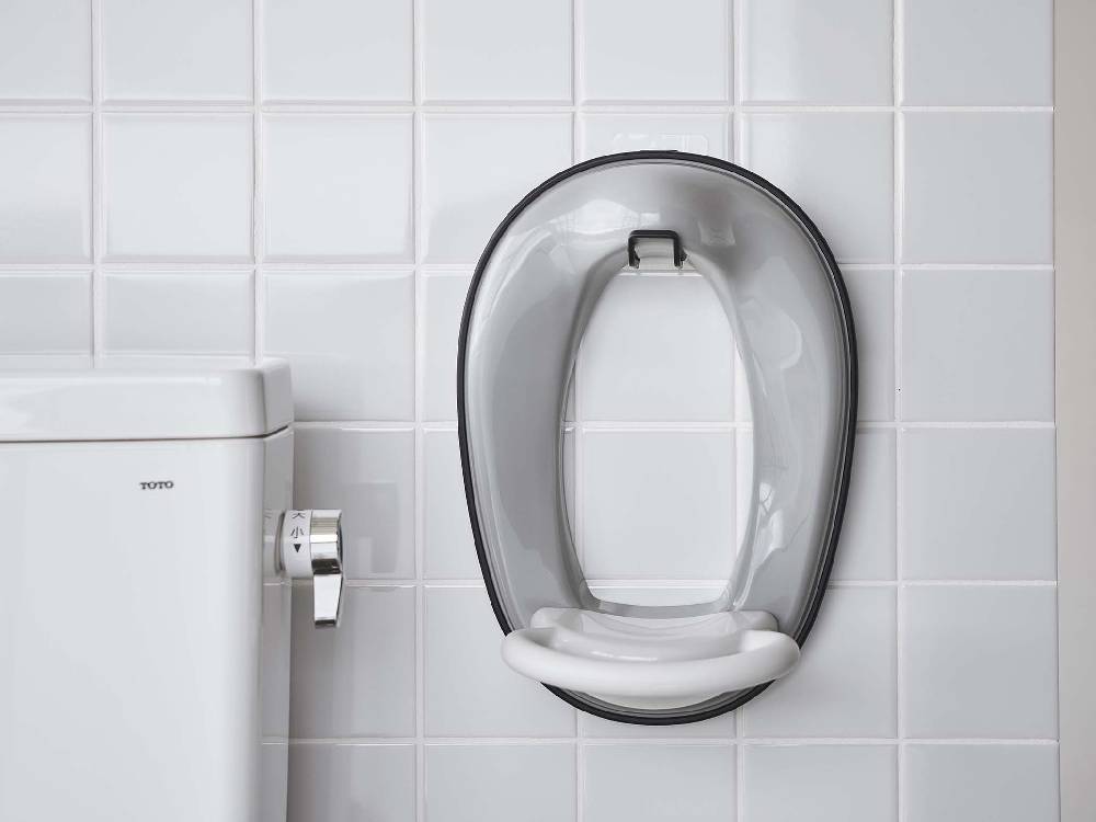 銀色のオーバル型フィルムフックがトイレ便座に取り付けられたバスルームの様子。洗練されたデザインで清潔感のある配管器具と調和しています。