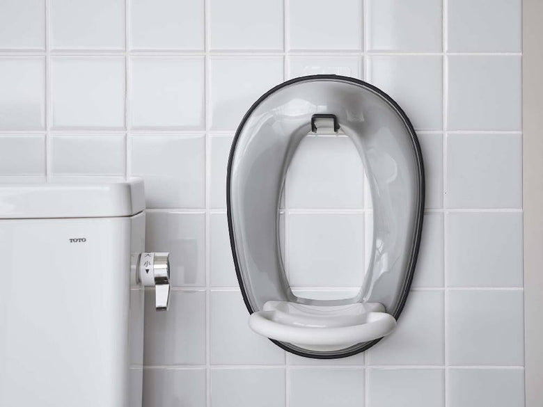 銀色のオーバル型フィルムフックがトイレ便座に取り付けられたバスルームの様子。洗練されたデザインで清潔感のある配管器具と調和しています。