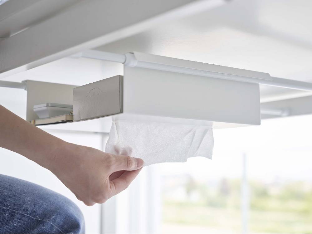 テーブル下に取り付けられたスチール製タワー型収納ラックに、紙タオルやティッシュペーパー、オフィス用品が整然と並べられている