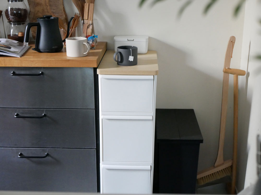 木製の天板が付いたスリムな収納ユニット。複数の引き出しが並び、上部には観葉植物やキッチン用品が置かれている