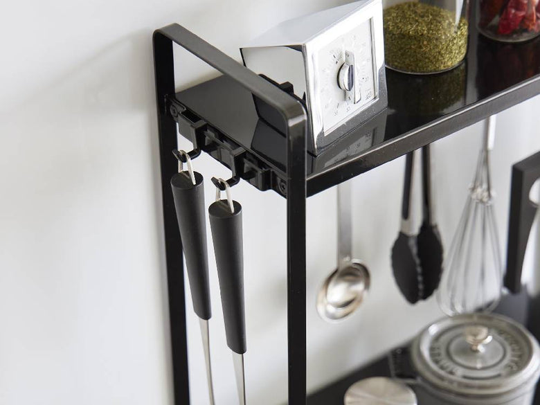 2段のタワー型コンロ横ラックにキッチン用品やグラス、カトラリーが整然と配置されたキッチンの様子