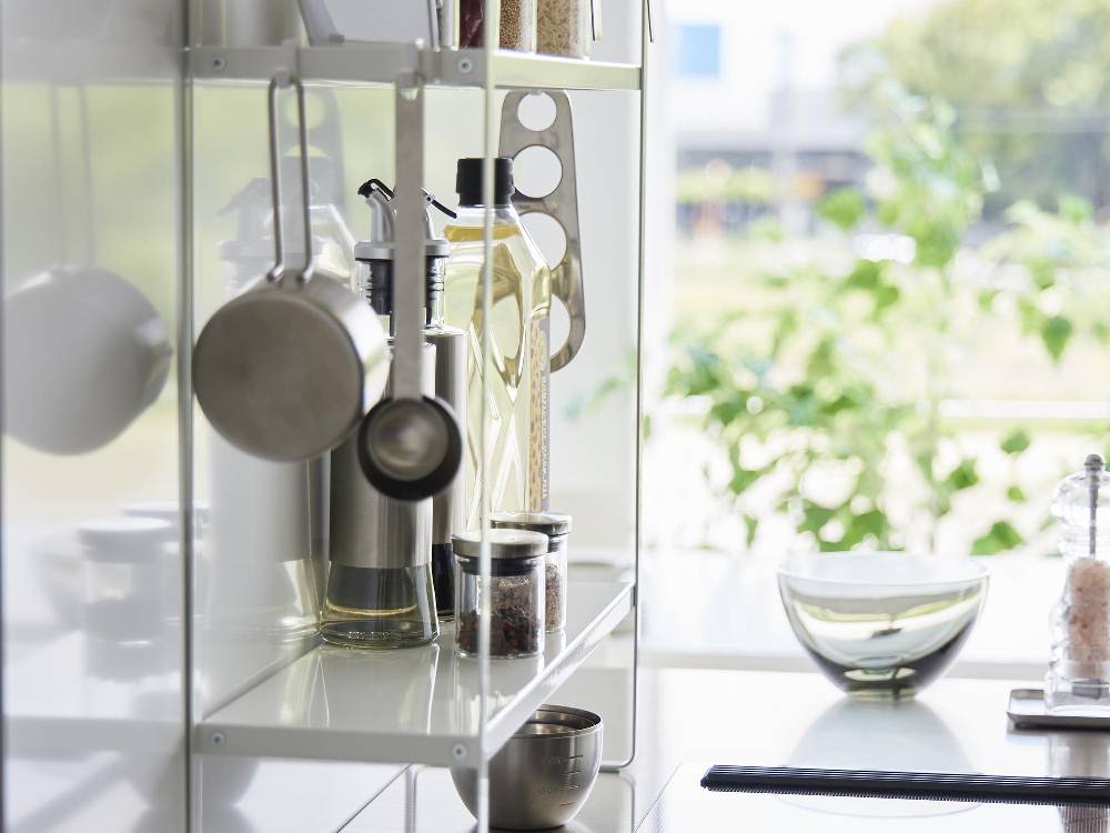 スチール製の2段コンロ横ラックがキッチンのカウンタートップに設置され、上段と下段の棚に食器や調理器具が整然と並べられている様子