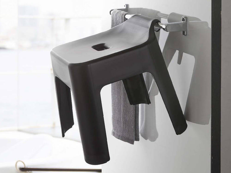 灰色と銀色のプラスチック製【tower/タワー】引っ掛け風呂イス SH30が木製の床の上に置かれ、隣にステップスツールが配置されている様子