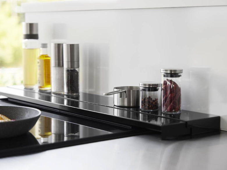 キッチンのコンロ上に取り付けられた75cm用奥行伸縮排気口カバー。スチール製でシリコーン滑り止め付き。周囲にはキッチン家電や調理器具が配置されています。