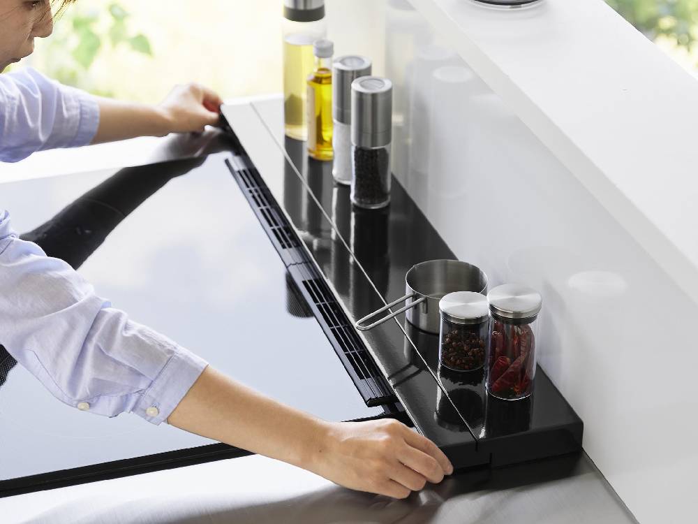 キッチンのカウンタートップに設置された75cmのタワー型伸縮排気口カバー。スチール製でシリコーン滑り止め付き、周囲に調理器具や果物などが配置されています。