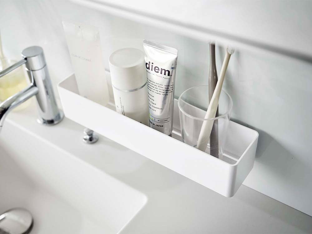 白色のフィルムフックラックが浴室のシンク上の棚に取り付けられ、ボトルや洗面用品が掛けられている様子
