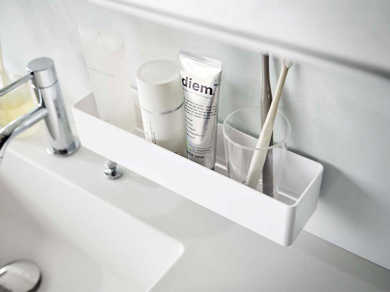 白色のフィルムフックラックが浴室のシンク上の棚に取り付けられ、ボトルや洗面用品が掛けられている様子