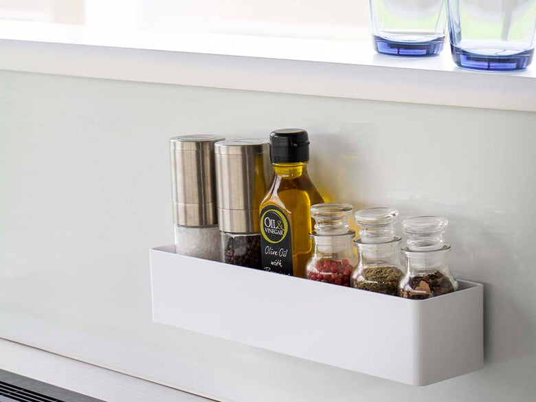 ホワイトのフィルムフックラックがキッチンの棚に取り付けられ、ガラス瓶や調理用具を整理している様子