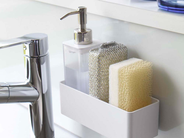 白いフィルムフックラックがバスルームのシンク横に取り付けられ、石鹸ディスペンサーや化粧品ボトルが掛かっている様子