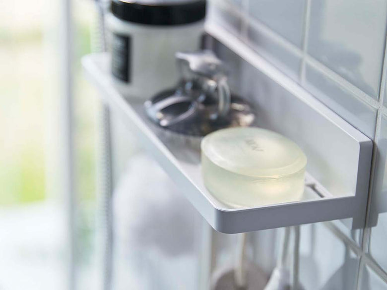 白いフィルムフックトレーが浴室の棚に設置され、タオルやボトルなどの家庭用品が整理されています