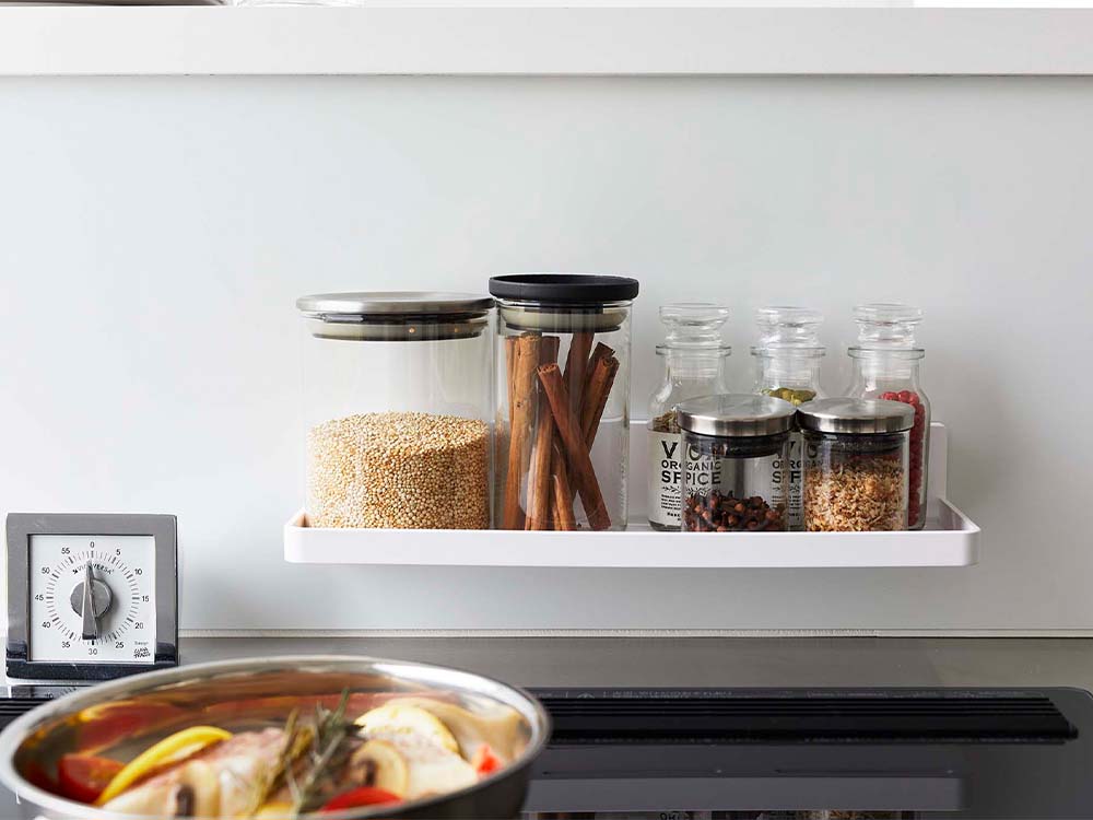 キッチンの棚にホワイトのフィルムフック付きトレーが配置され、食器や保存容器が整然と並んでいる様子