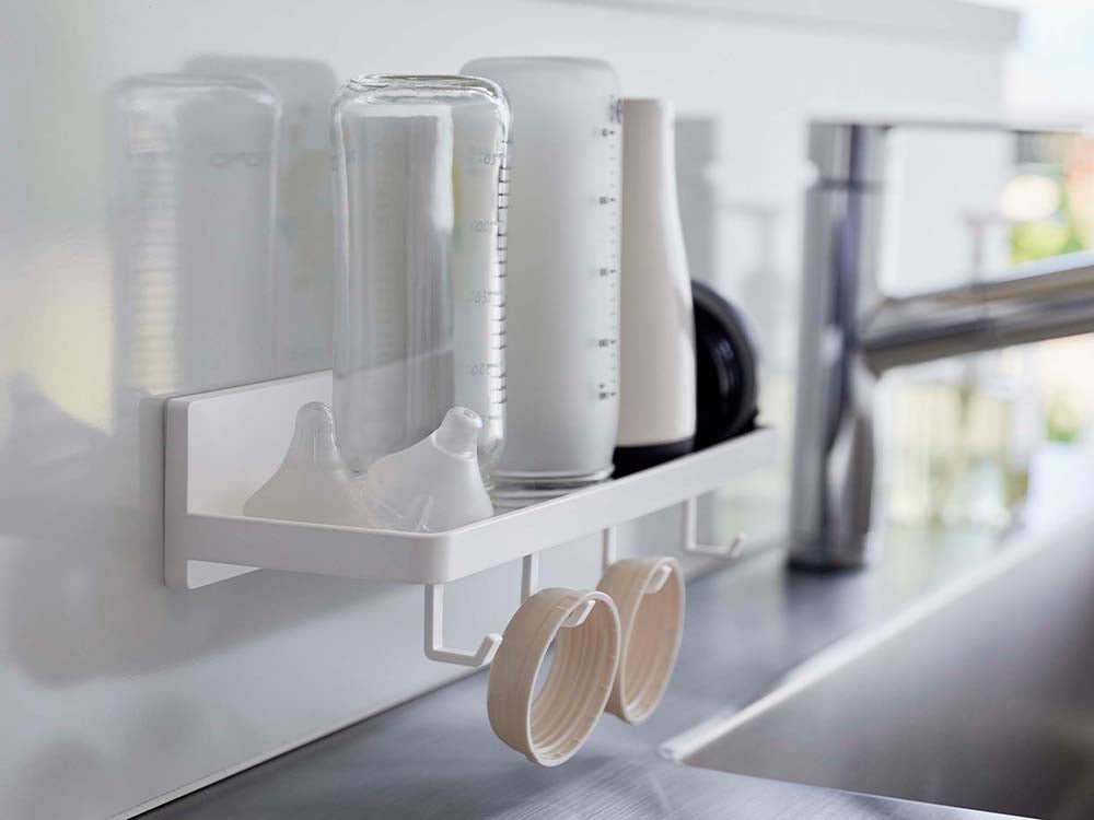 キッチンの棚に白色のフィルムフック付きトレーが配置され、調理器具や食器ラック、プラスチック製ボトルなどが整然と並んでいる様子