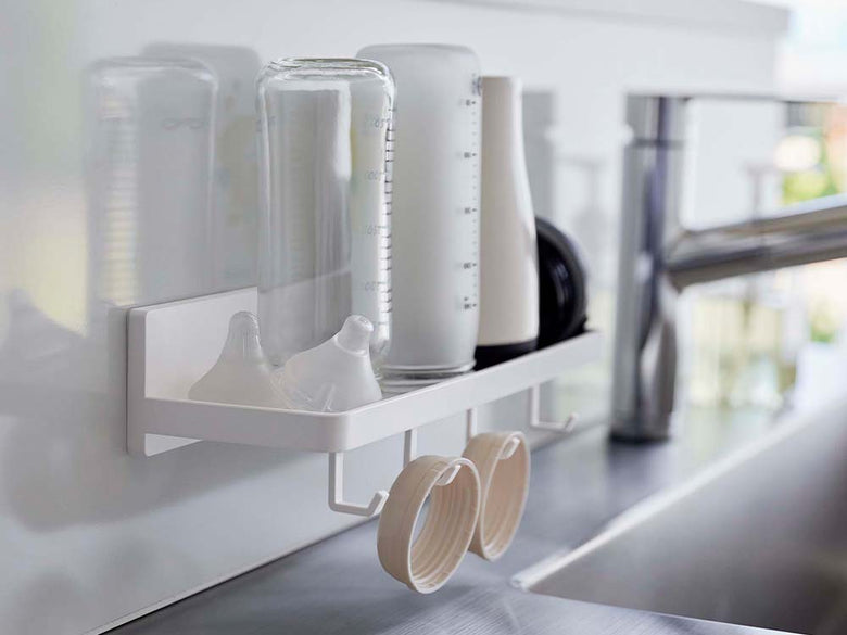 キッチンの棚に白色のフィルムフック付きトレーが配置され、調理器具や食器ラック、プラスチック製ボトルなどが整然と並んでいる様子