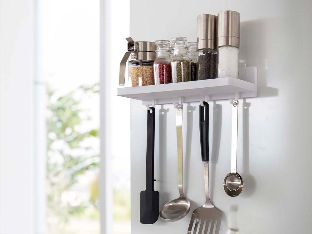 白色のフィルムフックトレーがキッチンの棚に設置され、調理器具やスパイスラックが整然と収納されている様子