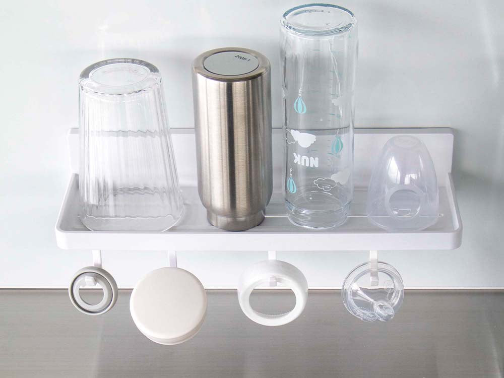 白色のフィルムフックトレーW30がキッチンの棚に取り付けられ、プラスチック製の調理器具や蓋を整理している様子