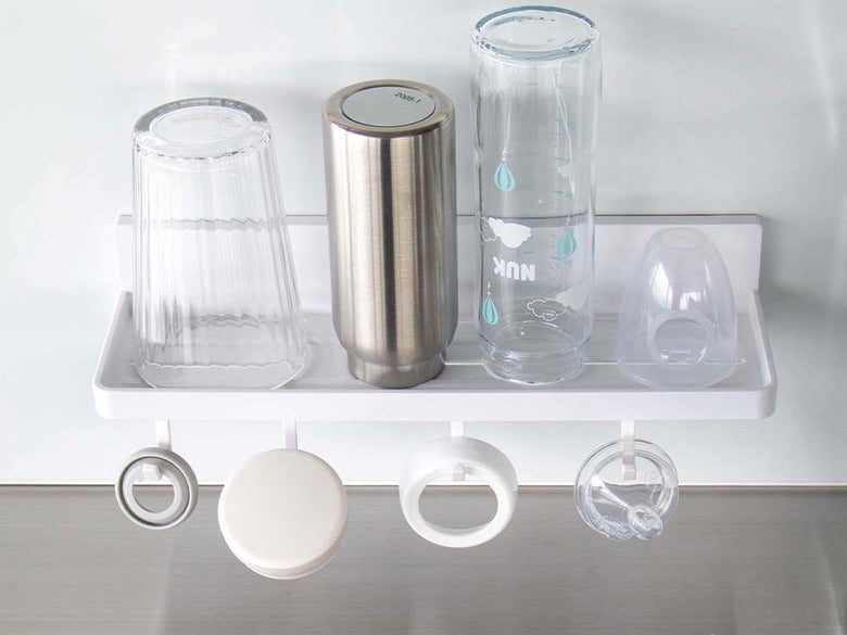 白色のフィルムフックトレーW30がキッチンの棚に取り付けられ、プラスチック製の調理器具や蓋を整理している様子