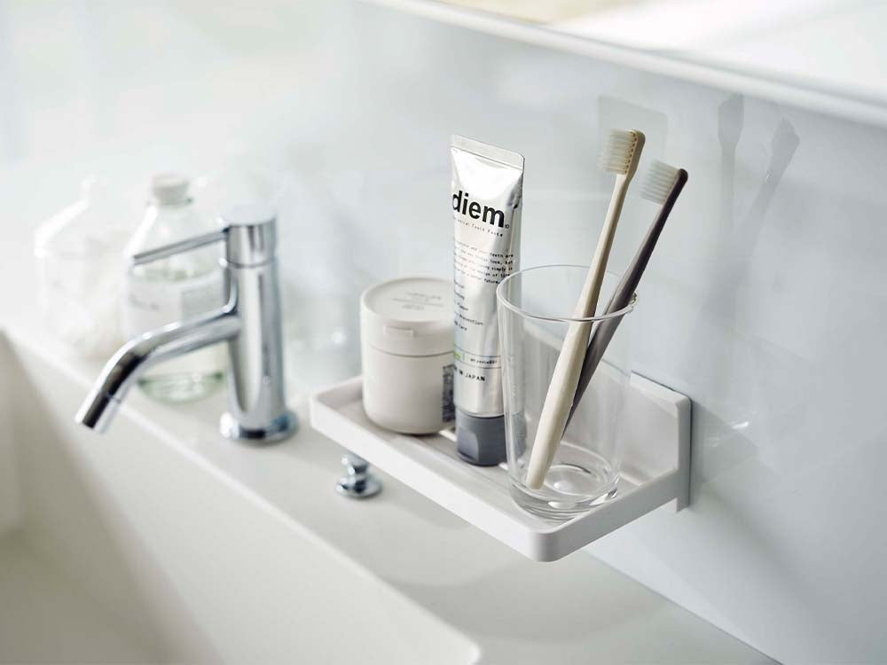 白色のフィルムフックトレーが洗面台に取り付けられ、シンクや蛇口、ソープディスペンサーなどのバスルーム用品が整理されている様子