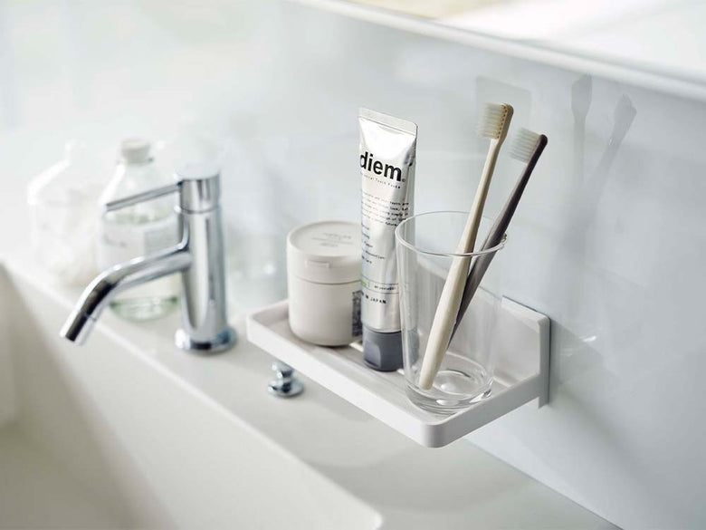 白色のフィルムフックトレーが洗面台に取り付けられ、シンクや蛇口、ソープディスペンサーなどのバスルーム用品が整理されている様子