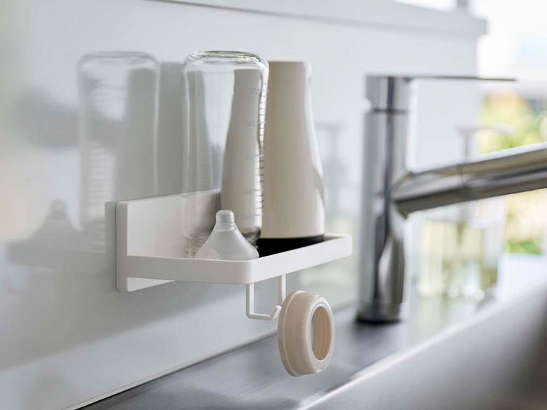 キッチンの棚に設置された白色のフィルムフックトレイ。シンクや蛇口などの家庭用品が整理されています。