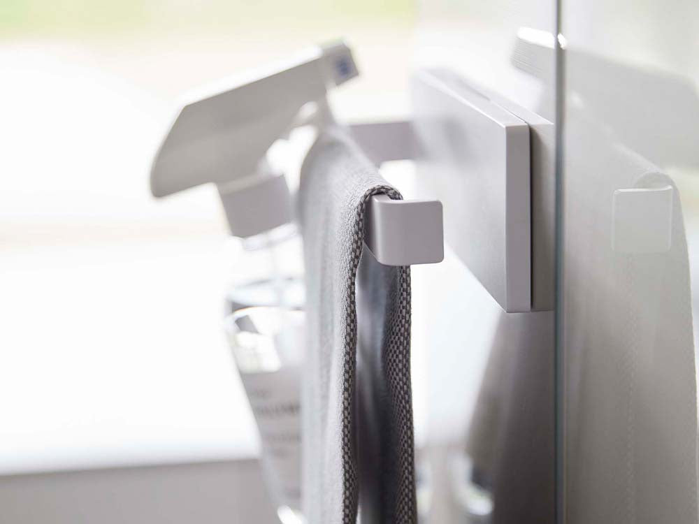 ホワイトのフィルムフックタオルハンガーが光沢のある平らな壁面に取り付けられ、タオルが掛けられている様子