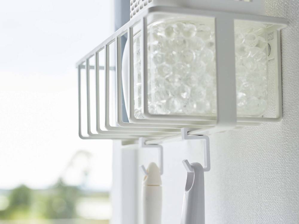 タワー型ウォールトイレ用品収納ラック。シルバーのスチール製棚にプラスチック製フックが2つ付いており、壁に取り付けられている様子。