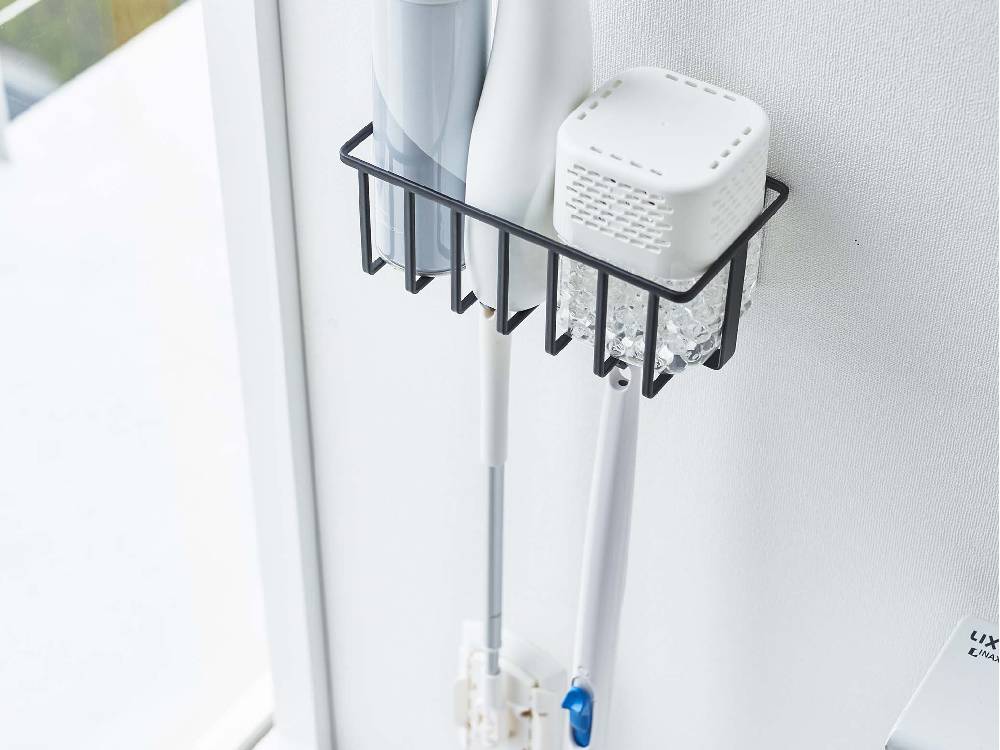 スチール製のウォールトイレ用品収納ラックが壁に取り付けられ、フックに歯ブラシやその他の日用品が掛けられている様子