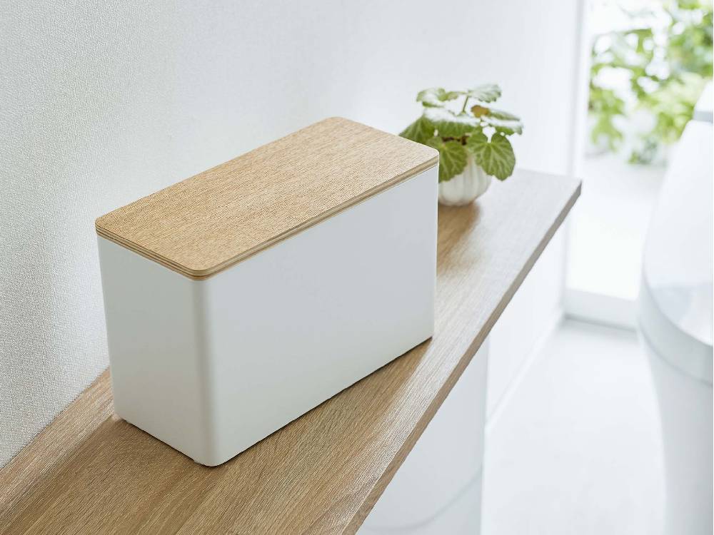 スチールと天然木で作られた【RIN/リン】分別サニタリー収納ホルダーが、ボックス、ラウドスピーカー、観葉植物と共に配置されている様子