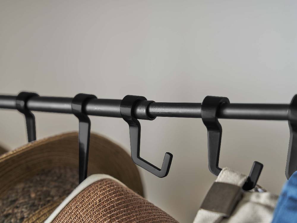 スチール製タワー帽子収納スタンドに衣類ハンガーが掛けられ、パイプとストラップで整理された様子