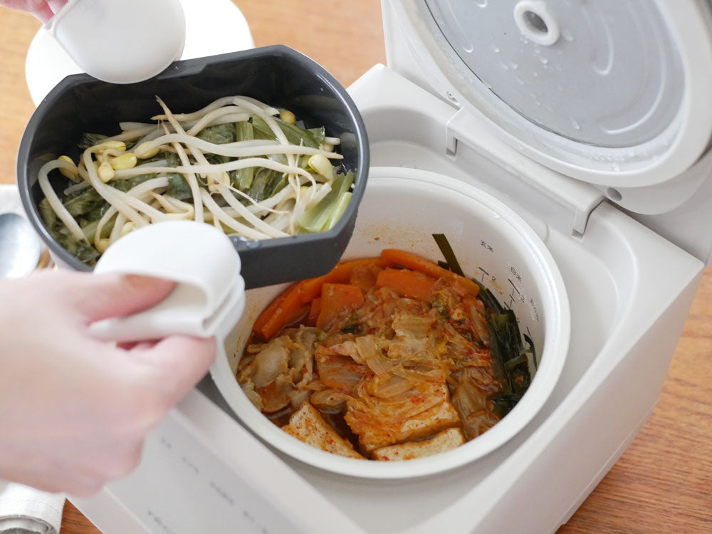 récolteクッキングライスクッカーと調理中の料理、周囲に野菜や食器が配置されたキッチンの様子