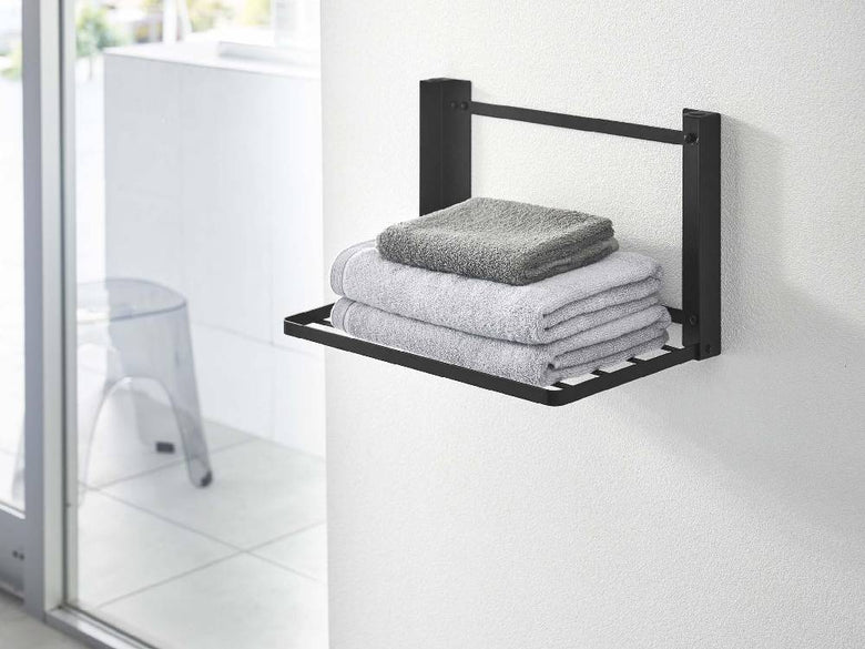 タワー折り畳み棚が浴室の壁に取り付けられ、紙タオルやタオルなどの家庭用品を整理している様子