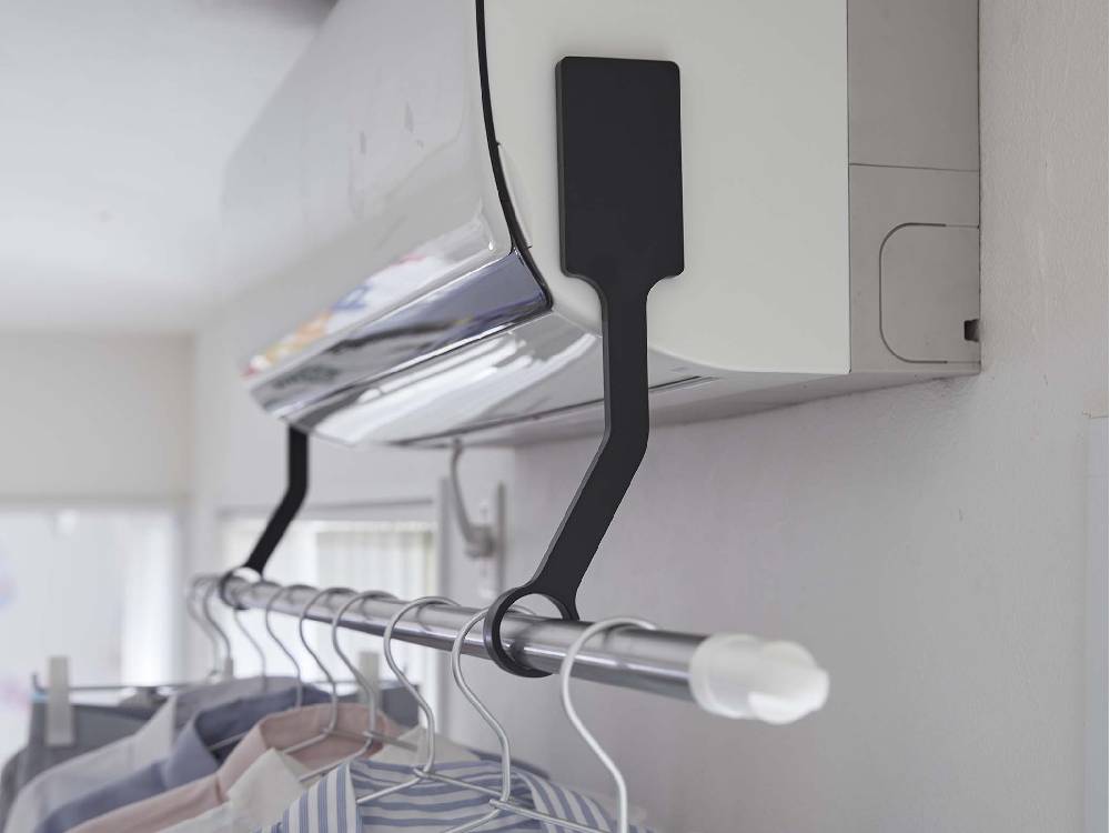 シルバーのタワーフィルムフックエアコン室内物干しポールホルダーが棚に取り付けられ、衣類ハンガーと電気ケーブルが配置された室内の様子