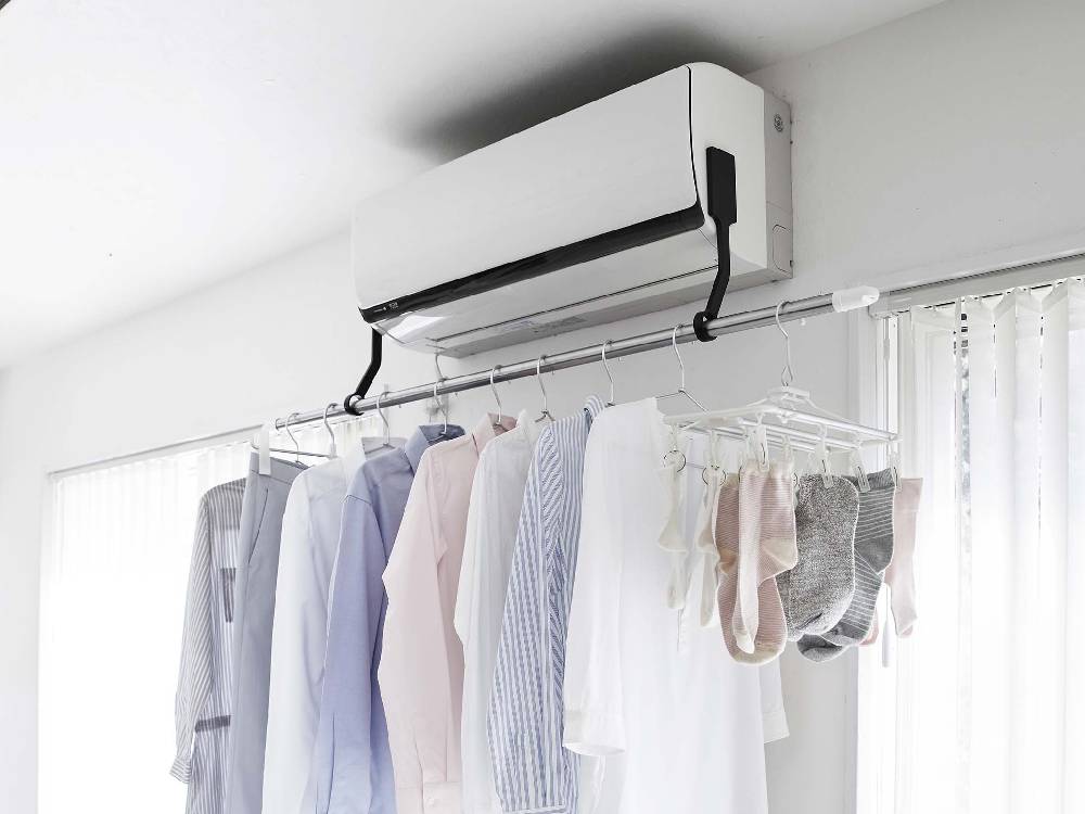 タワー型フィルムフックエアコン室内物干しポールホルダーがエアコンに取り付けられ、衣類を掛けている様子