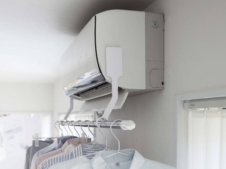 タワー製フィルムフックエアコン室内物干しポールホルダーが銀色のシェルフに設置され、電気ケーブルや家庭用品と共に配置されている様子