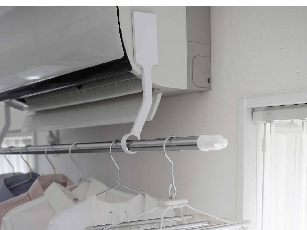 銀色のパイプに取り付けられたタワー型フィルムフックエアコン室内物干しポールホルダーに衣類が掛かり、電気ケーブルが整理整頓されている様子