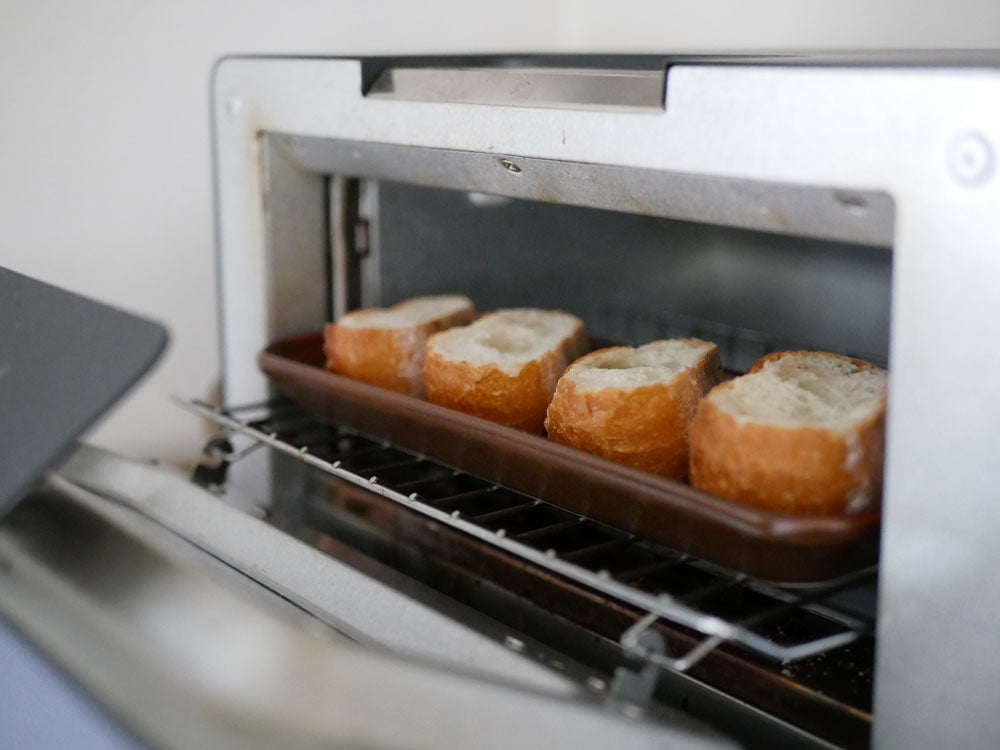 キッチンカウンターにトースターオーブンと電子レンジが置かれ、パンや調理材料が並ぶ調理風景