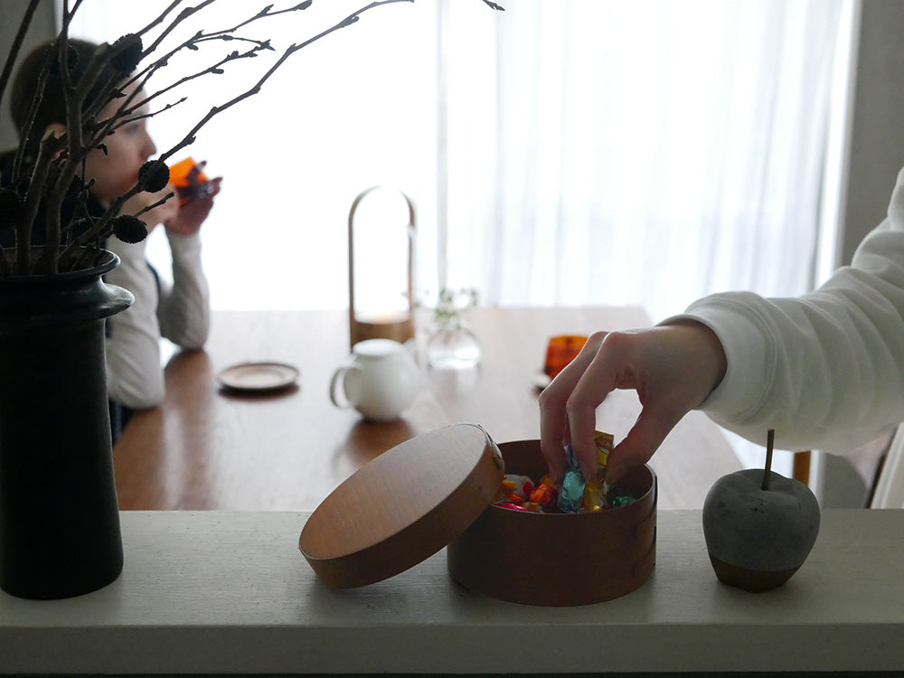 チェリー材製のアクシス シェーカーラウンドボックスと食器、フルーツ、花鉢がテーブル上に配置された様子