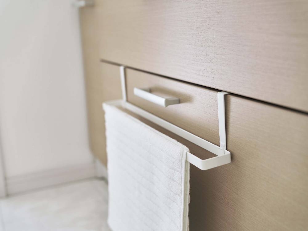 木製キャビネットの洗面下にスチール製の引っ掛けバスマットとタオルハンガーが設置されている様子