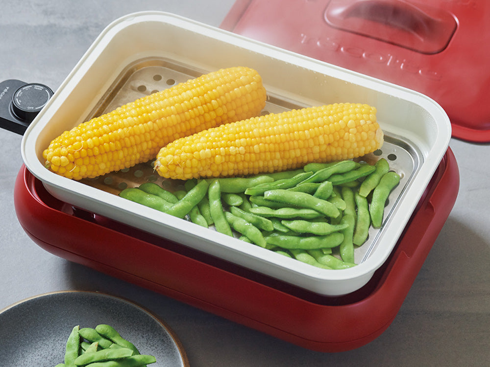 récolteの丸洗い可能なコンパクトホットプレート用セラミックスチーム深鍋セットと、野菜やキッチン用品がキッチンテーブルに整然と配置されている様子