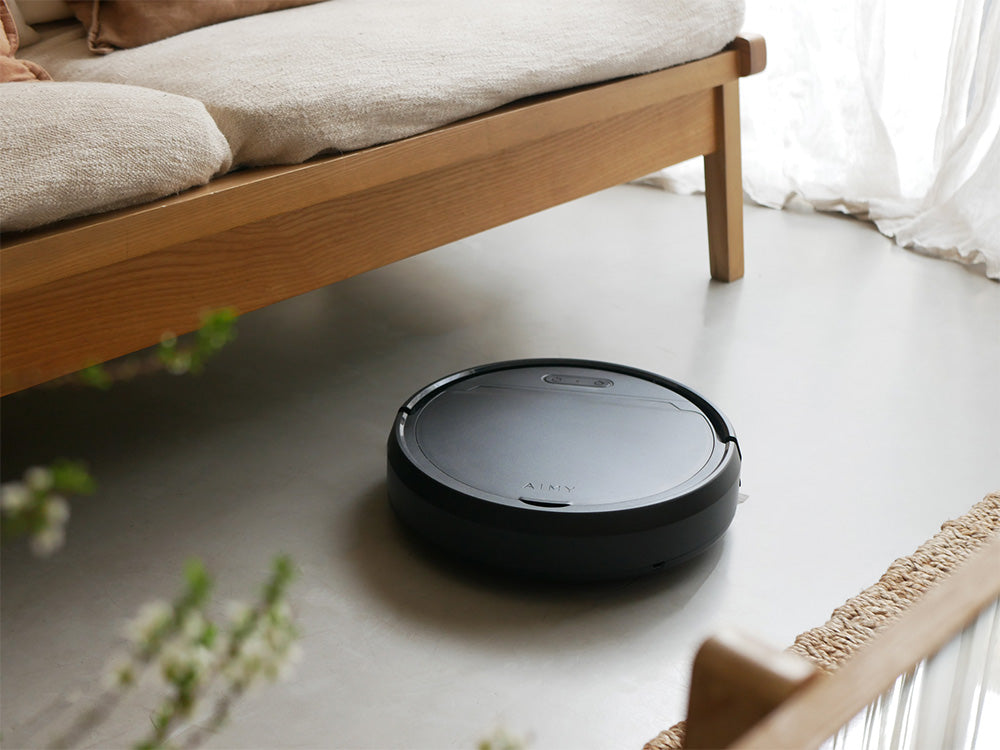 黒色の自動充電式ロボットクリーナー「AiMY/エイミー」が木製フローリングの上で清掃作業を行っている様子