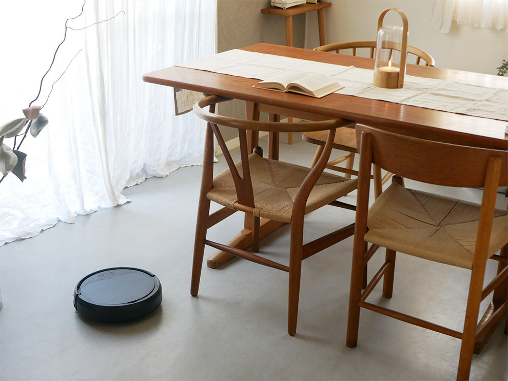 木製のフローリング上で黒色のAiMYロボットクリーナーが稼働中で、テーブルと椅子が配置されたキッチンダイニングルームの様子