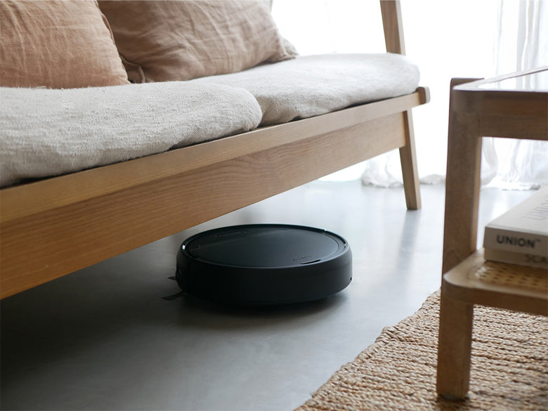 木製の床上で掃除中の黒いAiMYロボットクリーナーとスピーカー