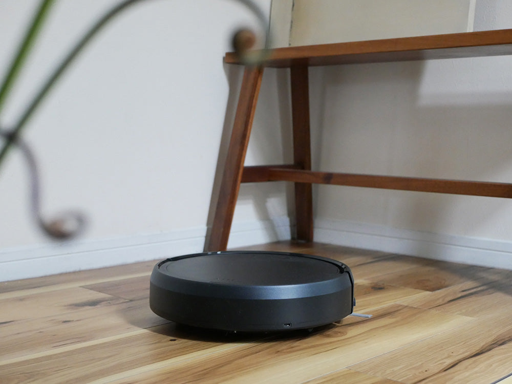 黒色のエイミー ロボットクリーナーが木製の床で自動的に掃除を行っている様子