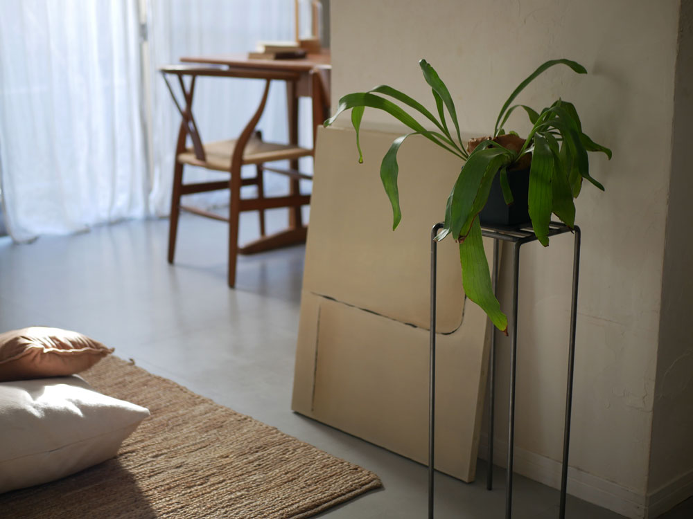 ウエストビレッジトーキョーのアイアン製プラントスタンドが木製フローリングの上に配置され、鉢植えとともにスタイリッシュなインテリアを演出している様子