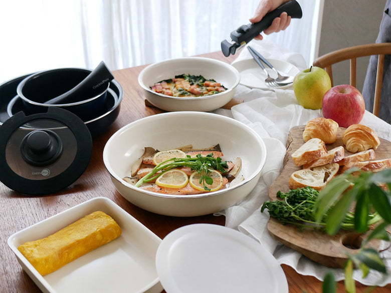 グリーンパンの取っ手が外せるクリックシェフの調理器具と食器がテーブル上に並び、野菜やキッチン用品が周囲に配置されている