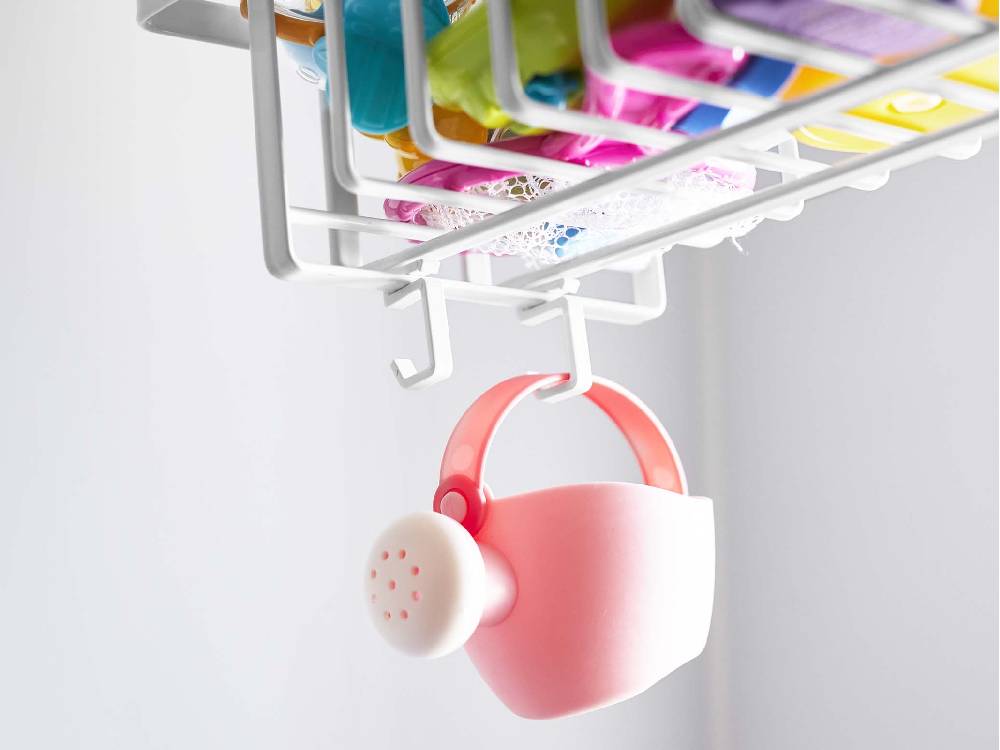 ピンク色の引っ掛けバスルームバスケットが棚に取り付けられ、日用品やキッチン用品を整理している様子