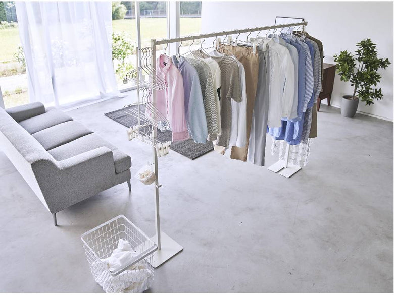 シルバー色の折り畳み式室内物干しタワーが自然素材風の床に設置され、アルミ製のハンガーが複数掛かっているデザイン