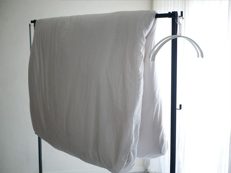 グレーとシルバーの折り畳み室内物干しタワーにハンガーやカーテン、タオルが掛かった様子